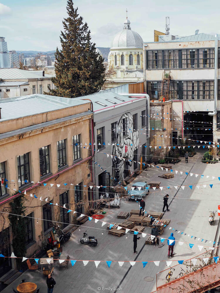 A concrete courtyard with a domed building in the background and bunting flags stretched between the buildings.