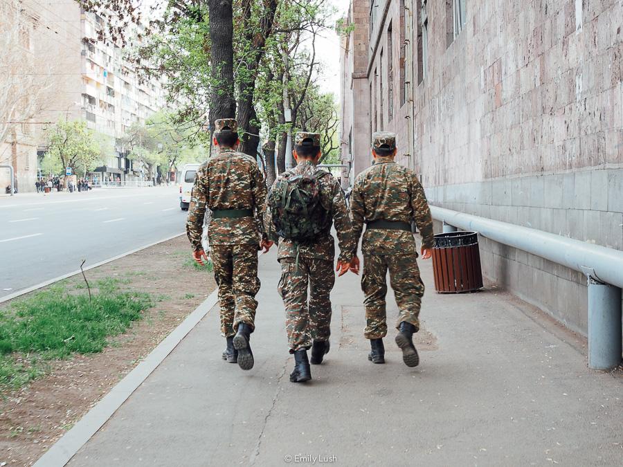 Three men dressed in soldier's uniforms walk down a concrete sidewalk in Yerevan, Armenia.