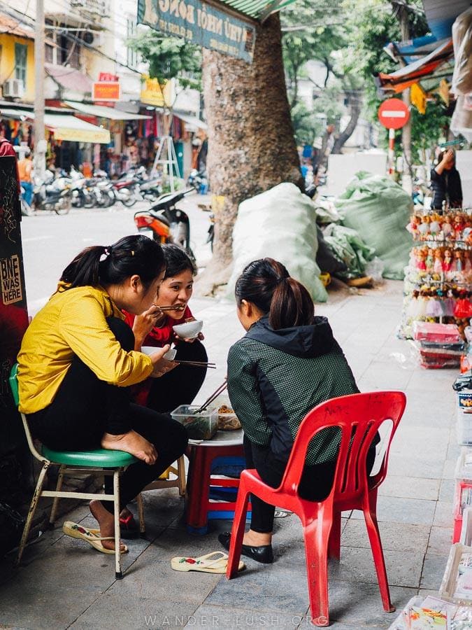 Three women eat noodles on the street in Hanoi Old Quarter.