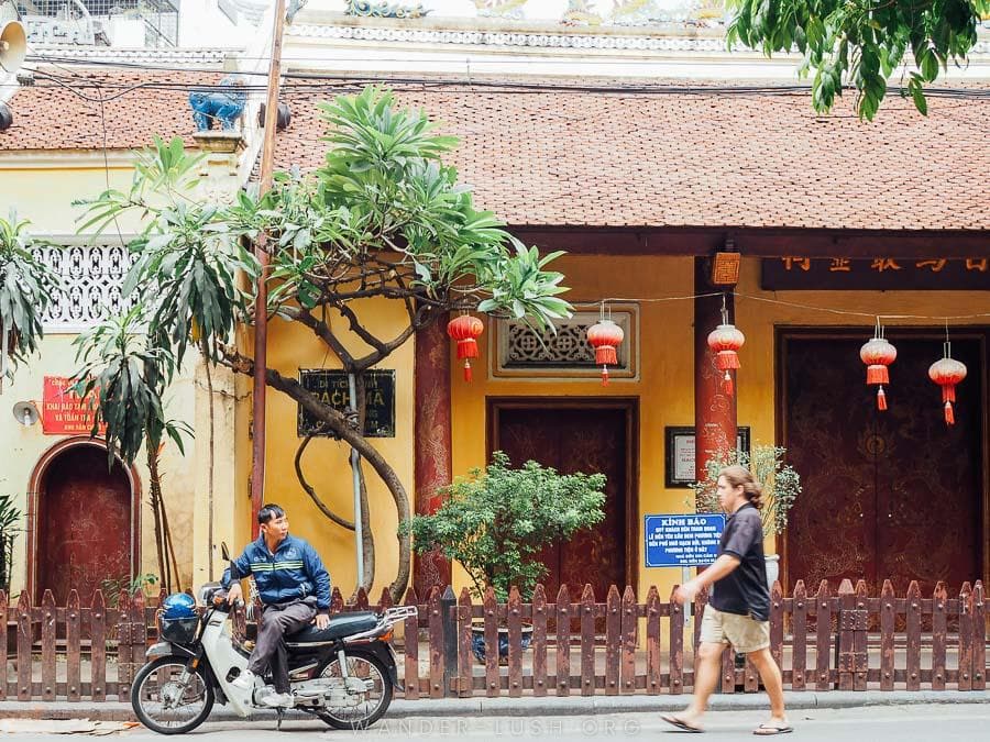 A tourist walks past a yellow building in Hanoi Old Quarter.