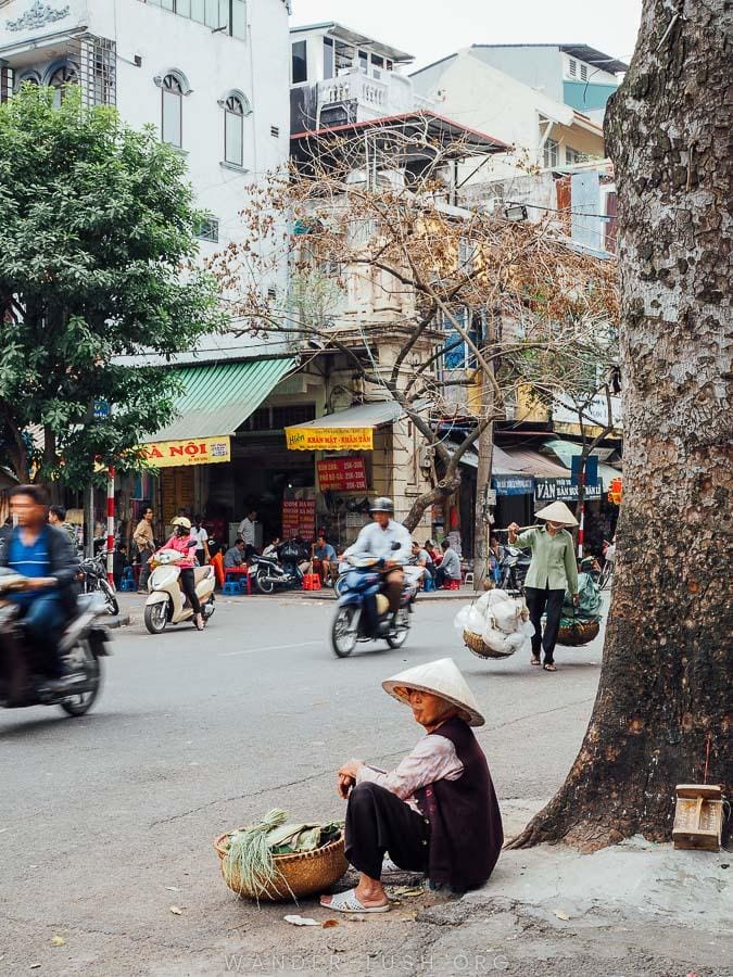 A woman sits in front of a large tree in Hanoi Old Quarter.