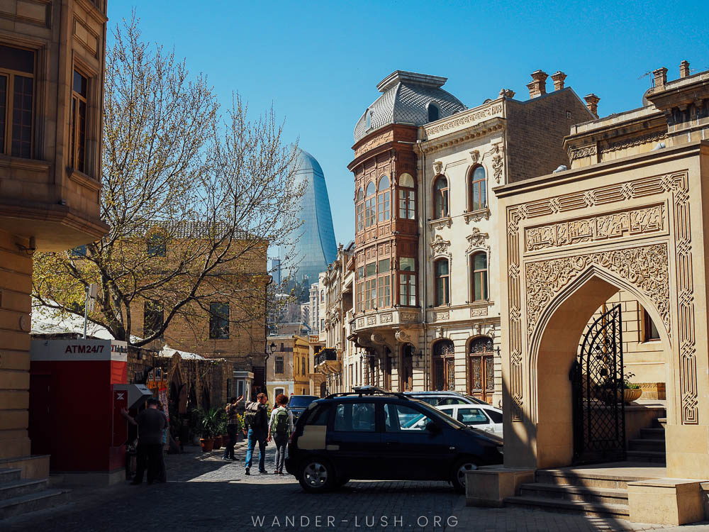 Two people walk through Baku Old Town, with a mix of old and new buildings.