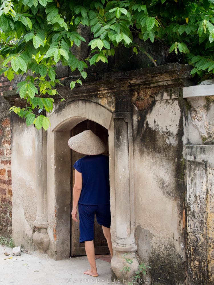 A woman in a conical hat looks out her doorway in Duong Lam Ancient Village near Hanoi.