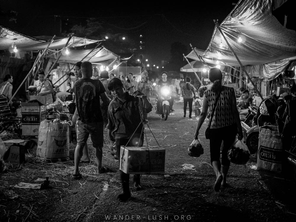 Vendors carry fruit and veg in baskets through a busy night market in Hanoi, Vietnam.