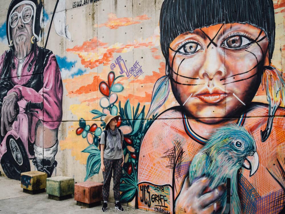 A woman in a hat looks up at a colourful street art mural in Comuna 13, Medellin.