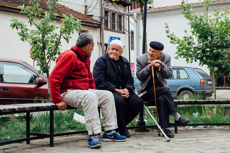 Three men sit on a seat outside a mosque in Kosovo.