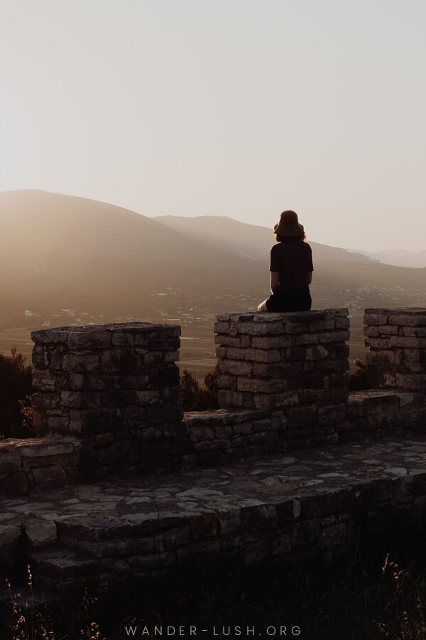 A woman sitting on the ruins of a stone castle at sunset.