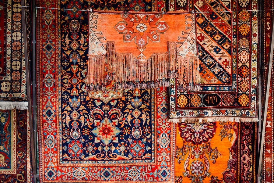 A display of red and pink-tone carpets with Caucasian designs.