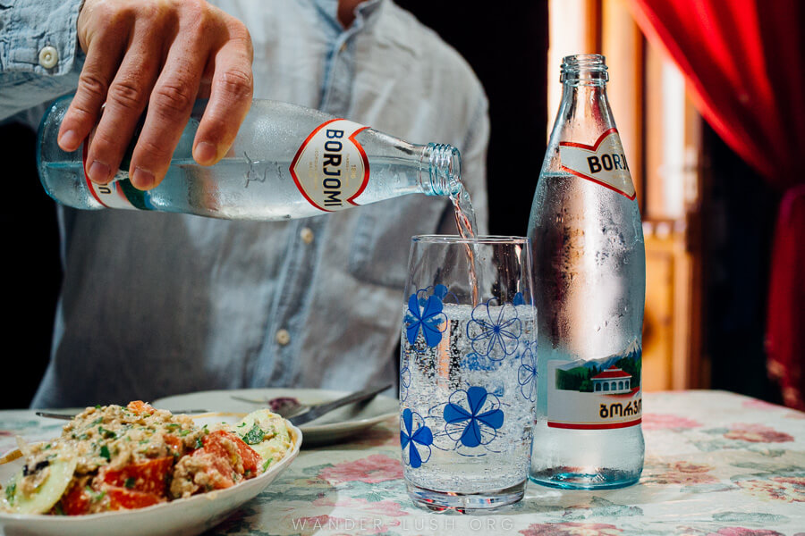 A man pours sparkling water from a bottle into a glass.