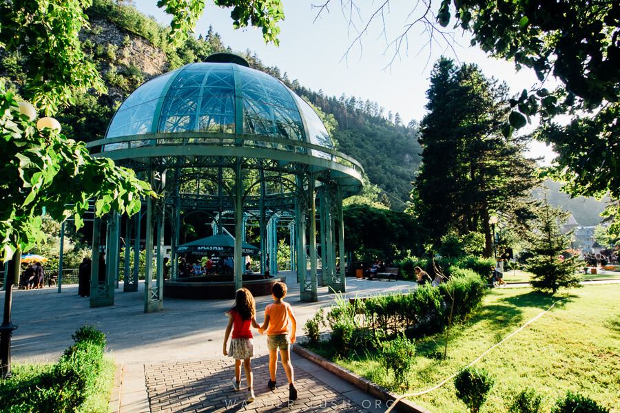 Two children walk towards a glass dome covering a mineral water spring in Borjomi, one of the best places to visit in Georgia (the country).