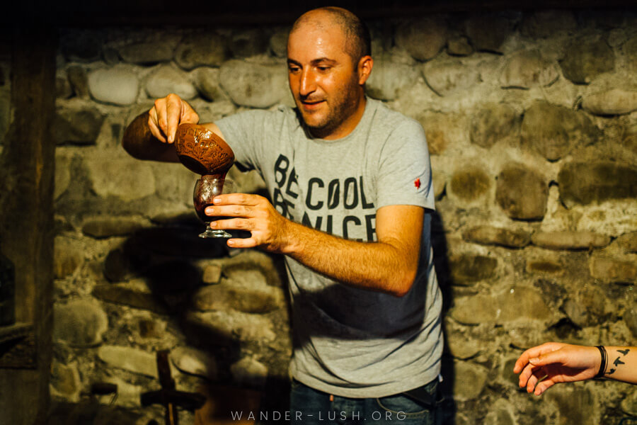 A man pours wine from a clay pot into a wine glass.