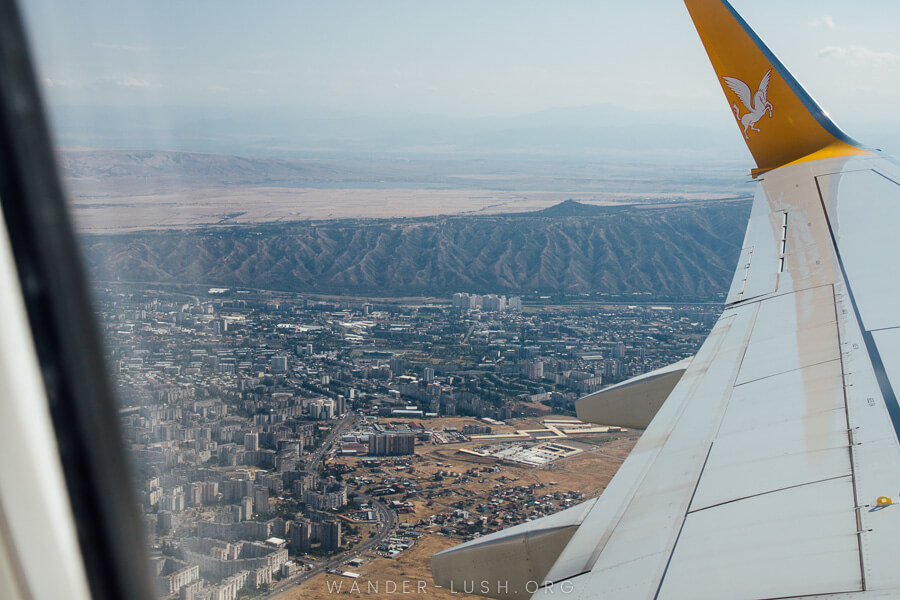 View of mountains and a city from an airplane window with the wing of the plane in the foreground. 
