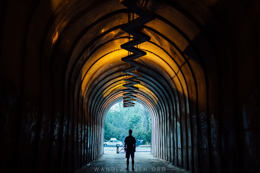 A man walks through a long, dark tunnel illuminated by a lightening-bolt light installation overhead.