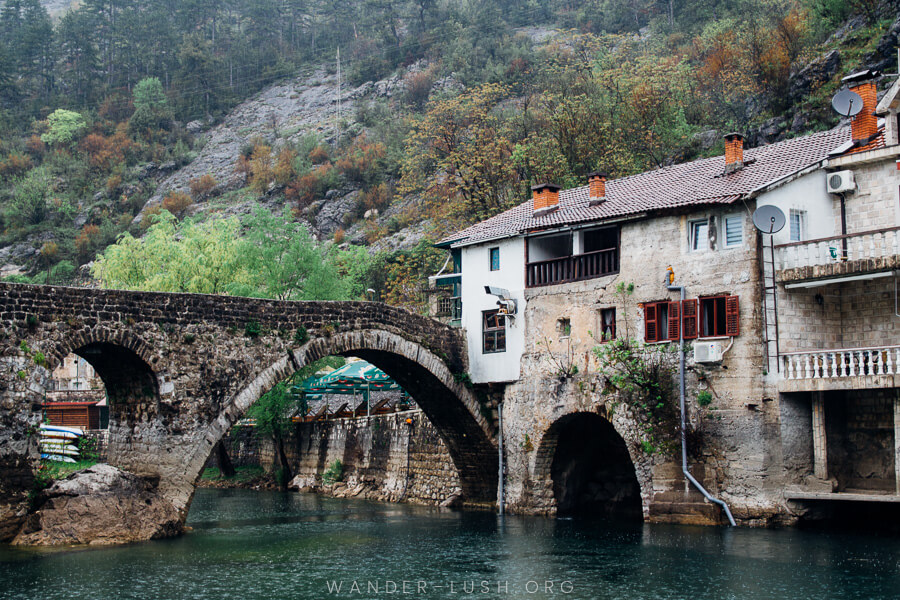 A very old stone bridge and stone houses overhanging a river.