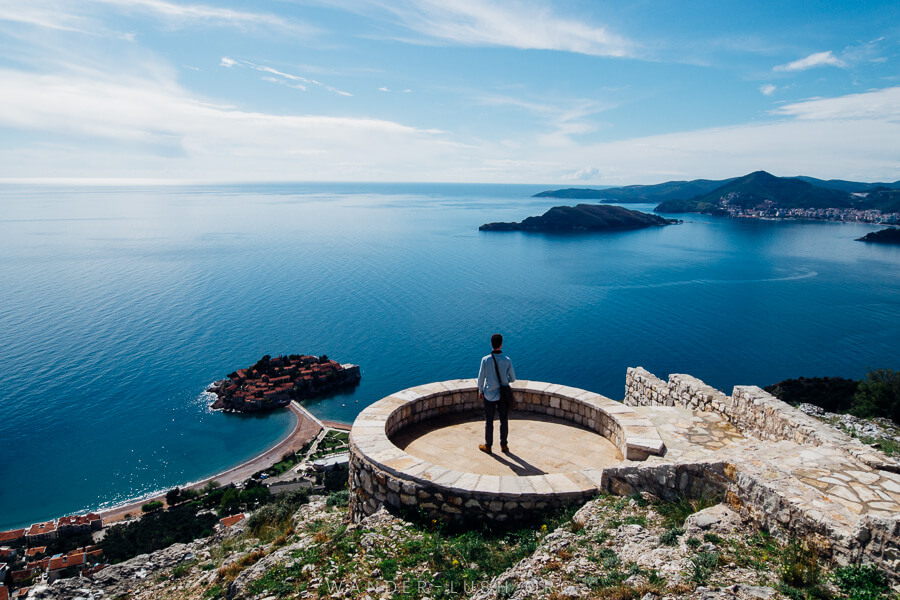 A person stands on a round viewing platform overlooking the ocean and a small island.