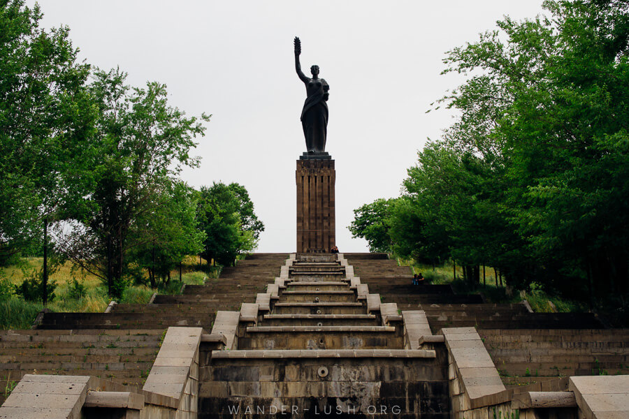 A statue of a woman atop of set of concrete steps.