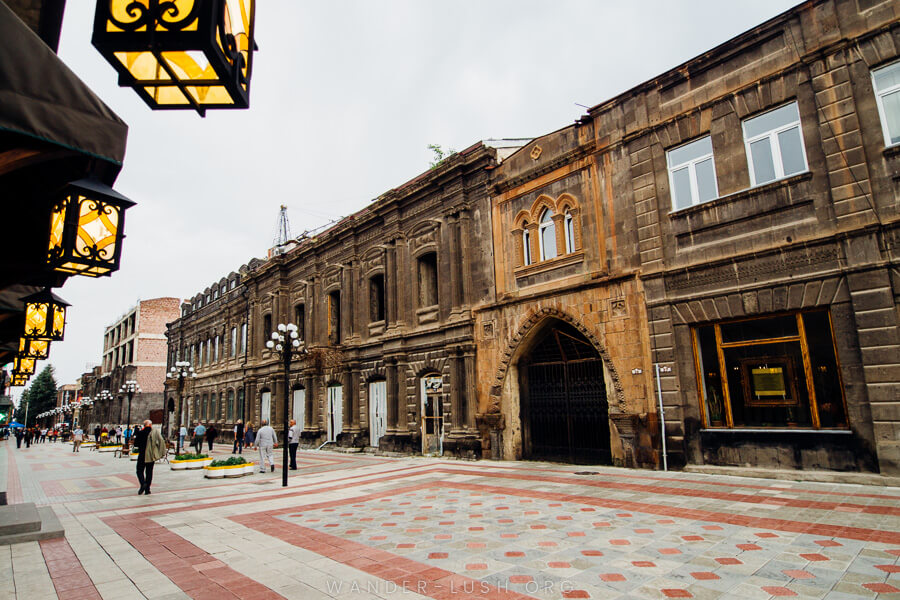 Stone buildings and a white-and-red tiled main street with pedestrians and lantern lights.