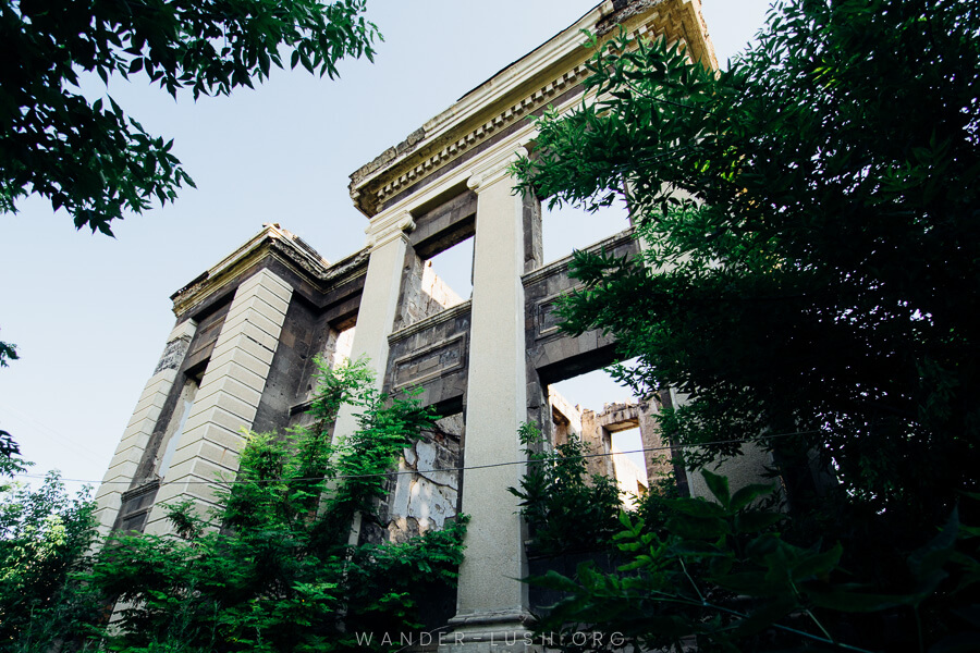 White brick pillars of a ruined building emerge from a green forest in Gyumri.