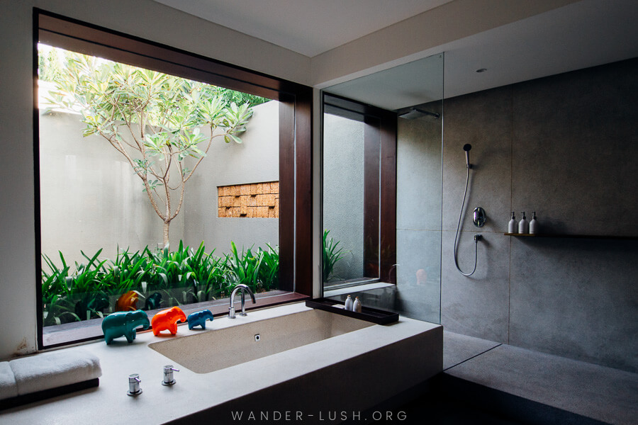 A concrete bathroom with large windows looking onto a garden.