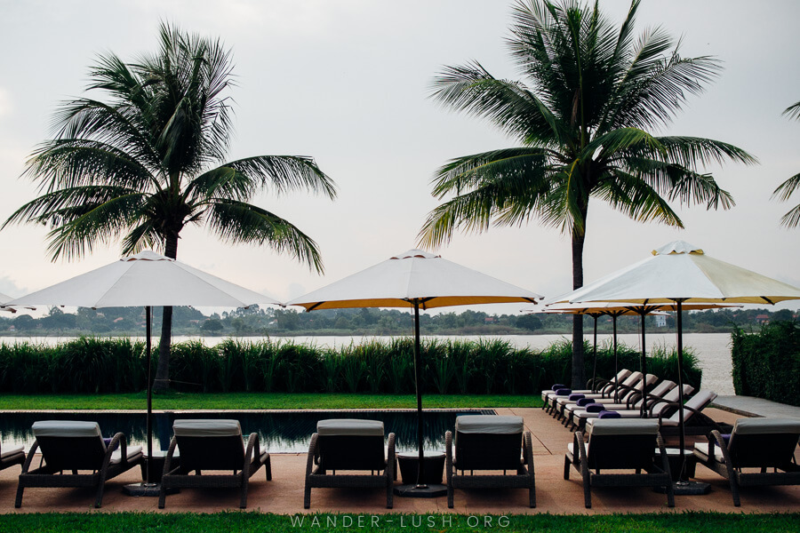 Deck chairs and umbrellas surrounding a pool with a river in the background.
