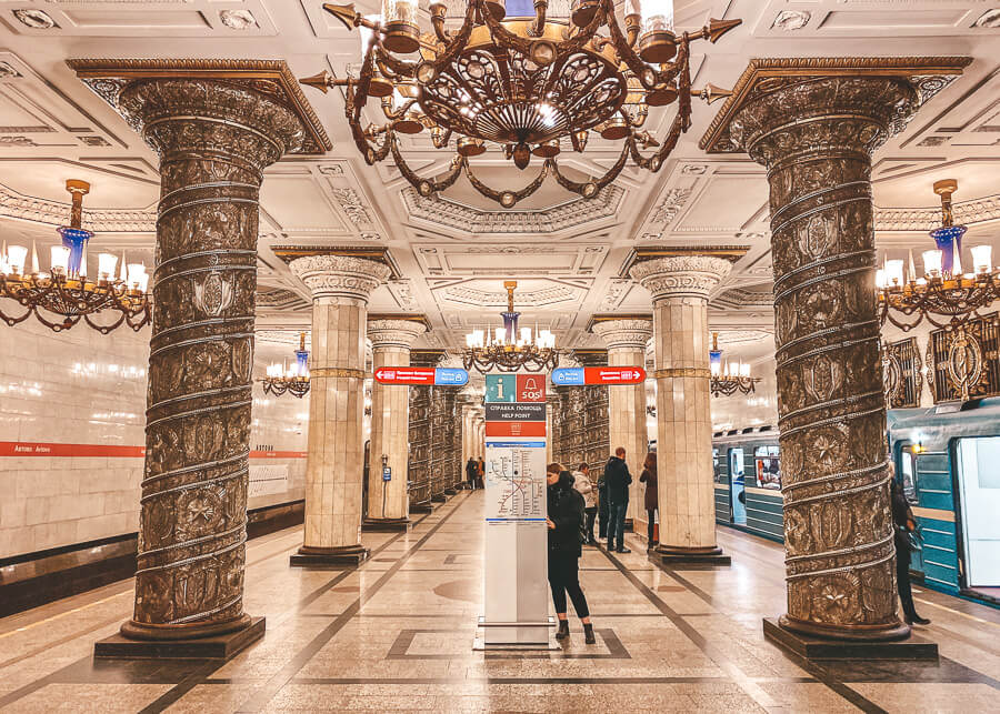 A woman reads a map inside St Petersberg metro station, with chandeliers hang from the ceiling and plaster moulding on the ceilings and columns.