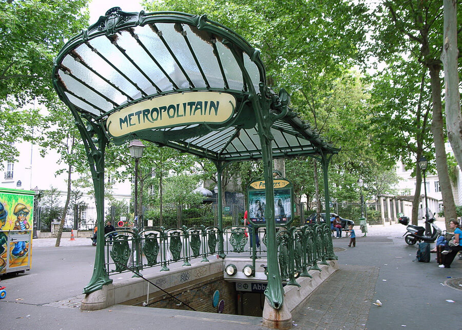 The outside of a metro station in Paris, with green wrought iron and a sign reading 'Metropolitain'.