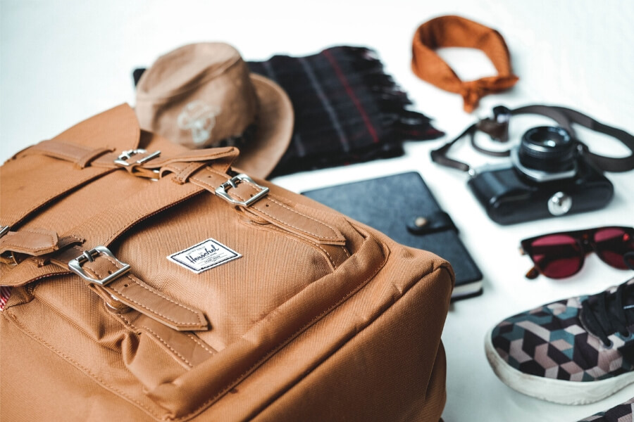 A brown backpack and a range of travel items ready to be packed.