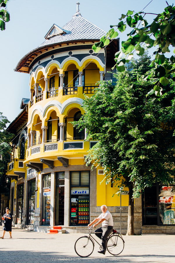 A man rides a bicycle in front of a yellow building in Korca, Albania.