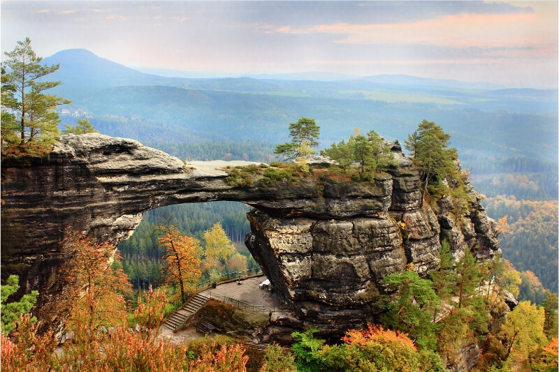 A natural stone arch surrounded by autumn foliage.