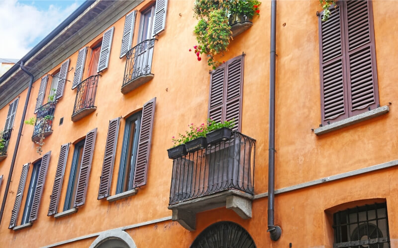 An orange house with wooden shutters and flower boxes in the colourful neighbourhoods of Milan.