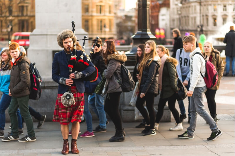 A man plays the bagpipes on a busy street in Scotland.