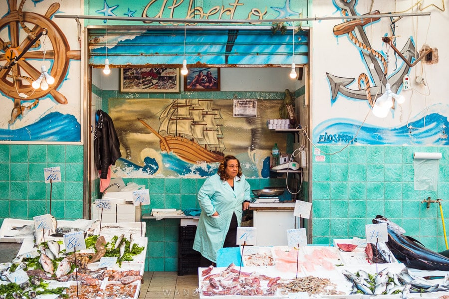 A woman standing in front of her seafood store in Naples, Italy.