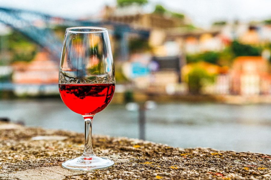A glass of Port Wine held up against a backdrop of the river in Porto, one of the best souvenirs from Portugal.