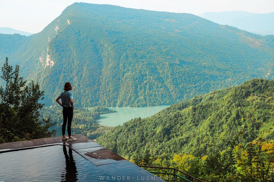 A woman stands at the edge of a pool overlooking a beautiful mountain landscape in Racha-Lechkhumi, Georgia.