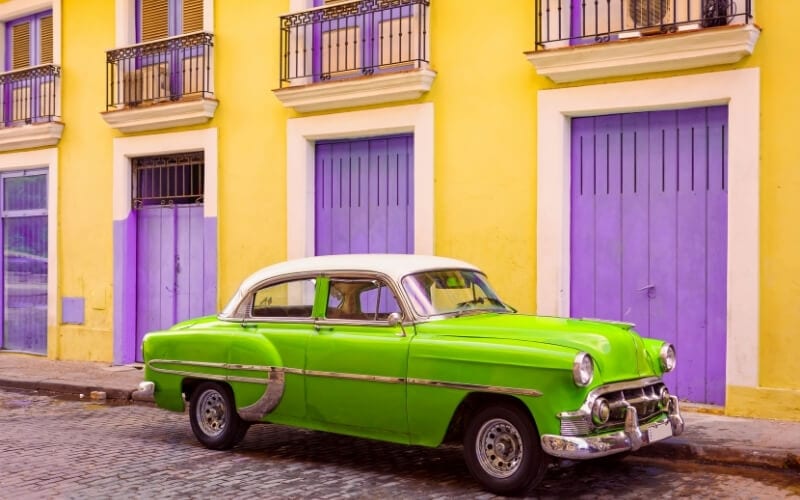 A colourful car parked in front of brightly painted houses in Cuba.