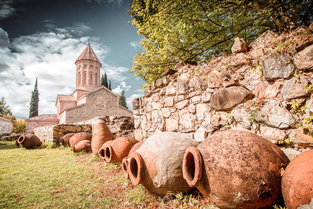 Clay qvevri jars lined up against a brick wall leading to a church in Kakheti, Georgia.