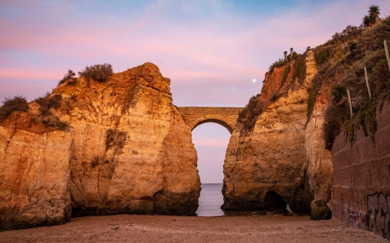 An old Roman bridge and rock formations at Praia dos Estudantes beach in Portugal.