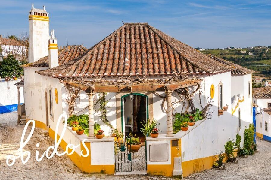A cute corner house decorated with white and yellow paint in Obidos, one of the most beautiful towns in Portugal.