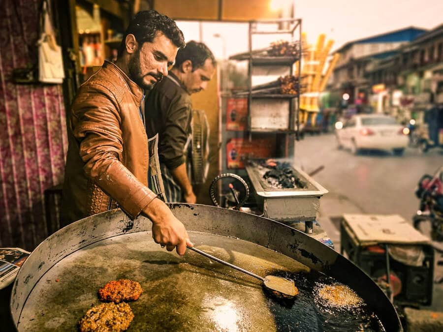 A man prepares traditional Pakistani street food in a large frying pan.