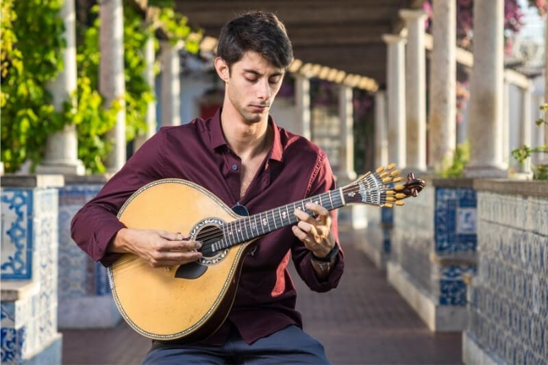 A man plays a traditional Portuguese guitar.