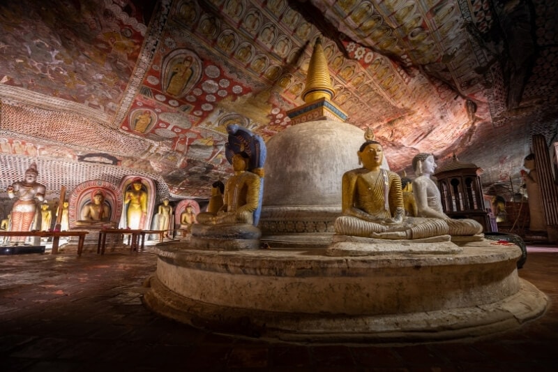 Buddha statues clustered around a stupa in a dark cave in Dambulla, Sri Lanka.
