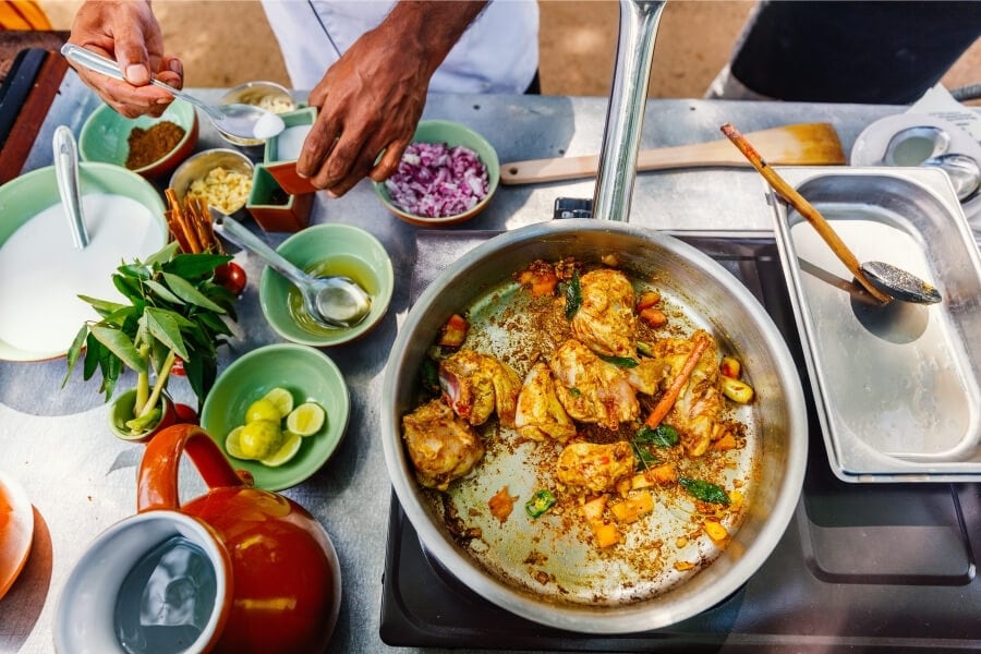 A man prepares a traditional Sri Lankan curry using various spices and fresh ingredients.
