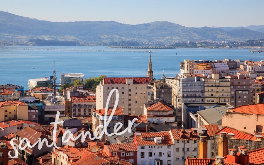 View of the port city of Santander, Spain, with colourful buildings, a church spire and a vast sea beyond.