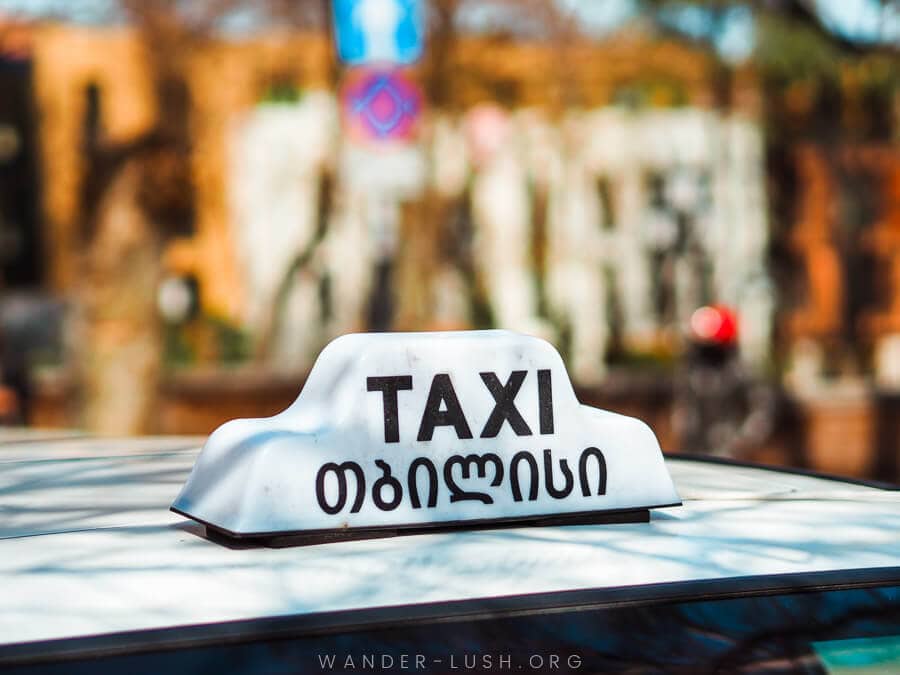 A cab on the street in Tbilisi with a standard 'Taxi Tbilisi' sign on top of its white roof.