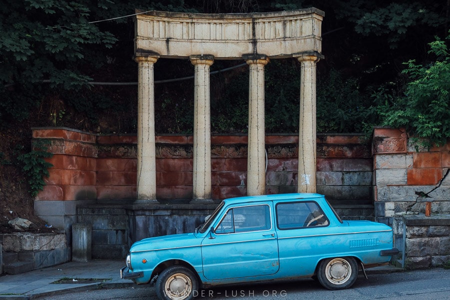 A decorative fountain in Dilijan, Armenia, with a retro blue car parke out front.