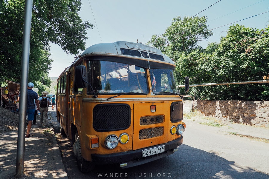 A bright yellow Soviet-era bus collects passengers on a street in Armenia.