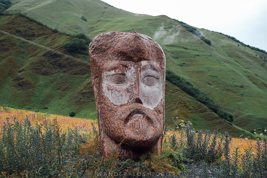 A giant stone head against a backdrop of green hills near Kazbegi in Georgia.