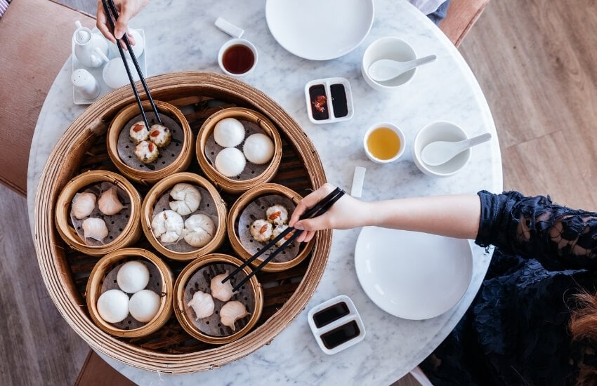 Two people eat dim sum from a large steamer basket.