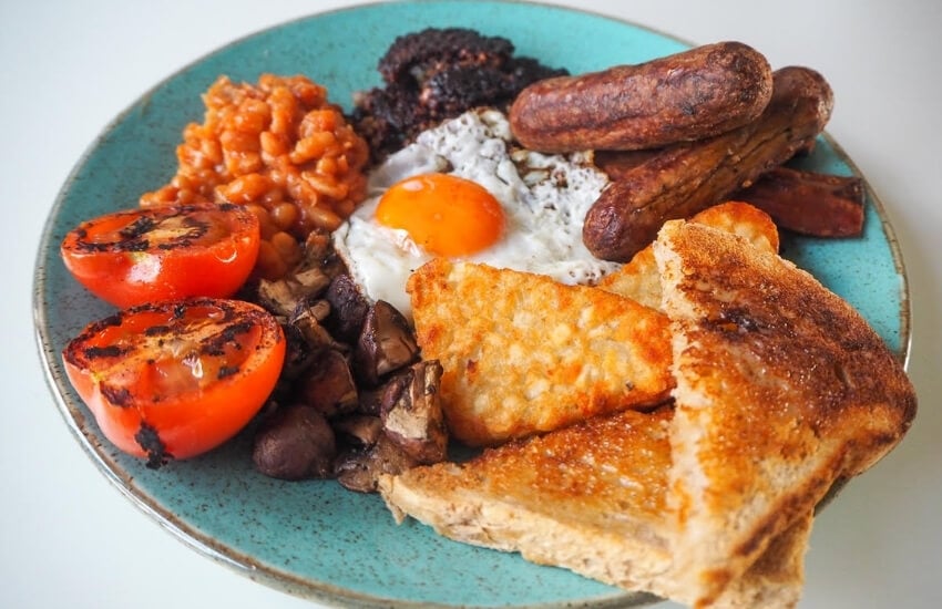 Toast, eggs and tomatoes on a green plate for a full English breakfast.