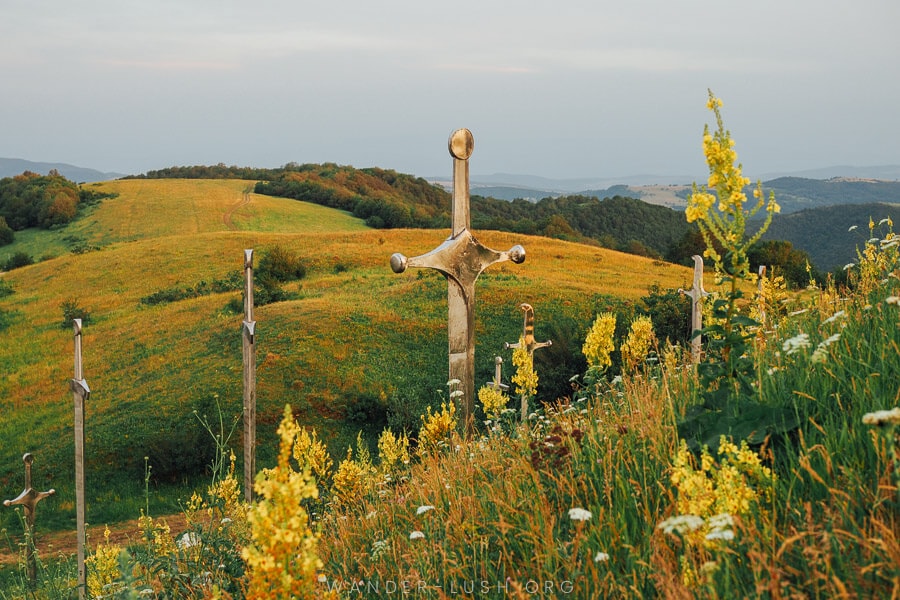 A green hill with yellow wildflowers and large metal sculptures.